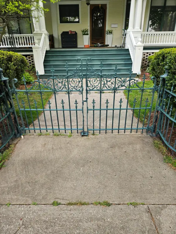 Restored green iron entry gate with scrollwork centered on a front walk to a Victorian porch