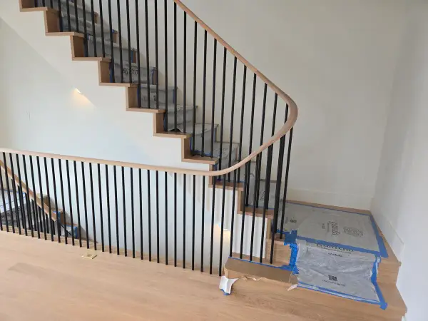 Curved staircase with thin black iron balusters and a continuous oak handrail in a new home